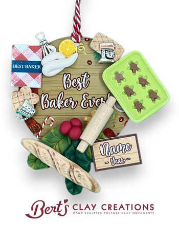 A handcrafted polymer clay ornament features a wooden sign reading “Best Baker Ever!” surrounded by miniature baking items: a gingerbread tray, cookbook, flour and sugar jars, rolling pin, bread, and a checkered cloth. A customizable nameplate at the bottom reads “Name Year.” The ornament hangs from a red and white striped string.